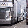 Convoy of big rigs semi trucks with semi trailers running on the highway in several lines