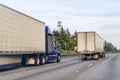 Convoy if big rig semi trucks with semi trailers transporting commercial cargo driving on the wide multiline highway road Royalty Free Stock Photo