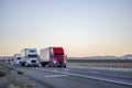 Convoy of industrial big rigs semi trucks with semi trailers driving with cargo on the straight highway road at twilight time Royalty Free Stock Photo