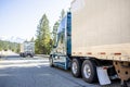 Convoy of the long haulers big rigs industrial semi trucks with semi trailers driving on the straight highway road with forest on Royalty Free Stock Photo