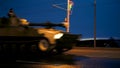 A convoy of military equipment rides through the city at night with headlights on