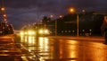 A convoy of military equipment rides through the city at night with headlights on