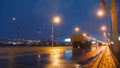 A convoy of military equipment rides through the city at night with headlights on