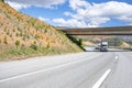 Convoy of two big rigs semi trucks with loaded semi trailers driving on the turning mountain highway road going under the bridge Royalty Free Stock Photo