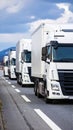 Convoy of white semi trucks driving down a highway under a cloudy sky Royalty Free Stock Photo