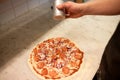 Cook adding pepper to salami pizza at pizzeria