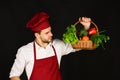 Cook in apron and hat looks at ingredients in hand.