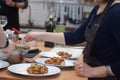 A cook in an apron sets the table, laying tomatoes in caprese salad with pesto