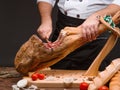 Cook in apron slicing spanish jamon on a wooden stand