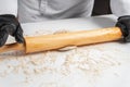 A cook in black gloves rolls out the dough with a wooden rolling pin Royalty Free Stock Photo