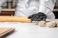 A cook in black gloves rolls out the dough with a wooden rolling pin Royalty Free Stock Photo
