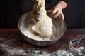 A cook in black kneads the dough in a metal bowl for cooking bread in the kitchen