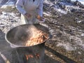 The cook cooks food on the street in a cauldron in winter on a bonfire and distributes it to the needy.