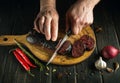 The cook cuts blood sausage with a knife on a cutting kitchen board. Cooking a national dish on the kitchen table with spices and Royalty Free Stock Photo