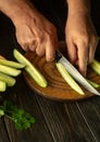The cook cuts the cucumber with a knife into lengthwise pieces for pickling. Work environment on the kitchen table with cucumbers
