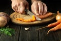 The cook cuts fresh carot on a wooden cutting board. Close-up of chef hands while preparing vegetarian food