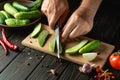 The cook cuts fresh cucumbers on a wooden cutting board. Close-up of chef hands while working on the kitchen table. Peasant food Royalty Free Stock Photo