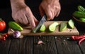 The cook cuts fresh green cucumbers on a wooden cutting board for preparing vegetarian food Royalty Free Stock Photo
