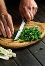 Cook cuts green onion leaves on a vintage cutting board before preparing a delicious dish or a vegetarian diet Royalty Free Stock Photo