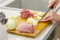 Cook cuts onions and raw meat on a wooden board