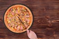 Cook cuts the pizza with a kitchen knife. Delicious pizza with chicken breast, corn, bacon and mushrooms on a round slate plate Royalty Free Stock Photo