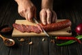 The cook cuts veal sausage on a wooden cutting board. Cooking delicious sandwiches for dinner on the kitchen table at home Royalty Free Stock Photo