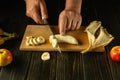 The cook cutting banana on a wooden boards. Low key concept of preparing a fruity breakfast dish on the kitchen table. Advertising Royalty Free Stock Photo