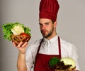 Cook with fresh vegetables. Chef with serious face holds vegetables