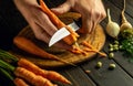 The cook hands with a knife peel the carrots on kitchen cutting board to prepare a vegetable meal