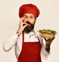 Cook with happy face in burgundy uniform holds baked dish. Royalty Free Stock Photo