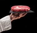 Cook holds graphite serving board with raw ribeye steak on black background