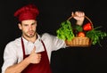 Cook holds vegetables in wooden basket showing thumbs up.