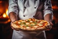 The cook holds a wood-fired pizza with cheese and herbs