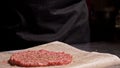 Cook makes meat medallions for burgers. Chef in black food gloves makes cutlet. Cutlets are leveled in steel ring in an