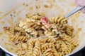 The cook mixes the pasta with a thick sauce and vegetables