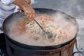 The cook mixes pilaf in a cauldron during cooking