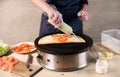 Cook pouring green sauce from bottle on pizza on portable cooktop. Ingredients for vegetarian pizza on wooden background Royalty Free Stock Photo