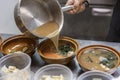 The cook pours the broth into the dishes in the kitchen of an Asian restaurant. Close-up