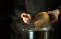 The cook pours dry buckwheat into the pan with a spoon. Dark space for recipe or menu. The idea of cooking delicious buckwheat