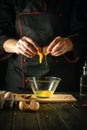 The cook pours a raw egg into a bowl. Delicious breakfast menu idea for hotel or restaurant on black background
