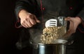 The cook pours Rolled oats from bowl into the pan. Dark space for recipe. The idea of cooking delicious porridge with oatmeal