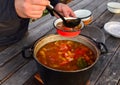 Cook, pours a tomato and pepper soup into a red plate from a large saucepan