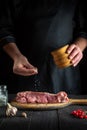 The cook prepares raw veal meat. Before baking, the chef adds salt to the beef. National dish is being prepared in the kitchen Royalty Free Stock Photo