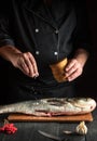 Cook prepares silver carp herring in the restaurant kitchen. Chef sprinkles salt on fish. Work environment on kitchen table Royalty Free Stock Photo