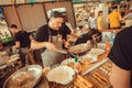 Cook preparing Asian food with spices and vegetables in a huge wok