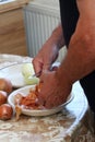 Man's hands peeling freh raw onion with kitchen knife on the kitchen table