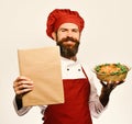 Cook with proud smile in burgundy uniform holds baked dish and menu. Man with beard isolated on white background. Chef