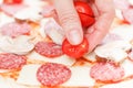 Cook putting tomato over mozzarella and salami on a raw pizza