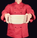 Cook in red uniform holds in his hands a stack of round white empty plates Royalty Free Stock Photo