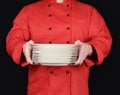 Cook in red uniform holds round white empty plates Royalty Free Stock Photo